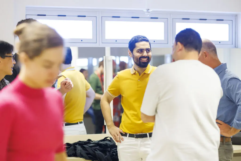 Danish Kazmi swearing a yellow polo stands smiling in the Green Room with other speakers at TEDxBrisbane 2022