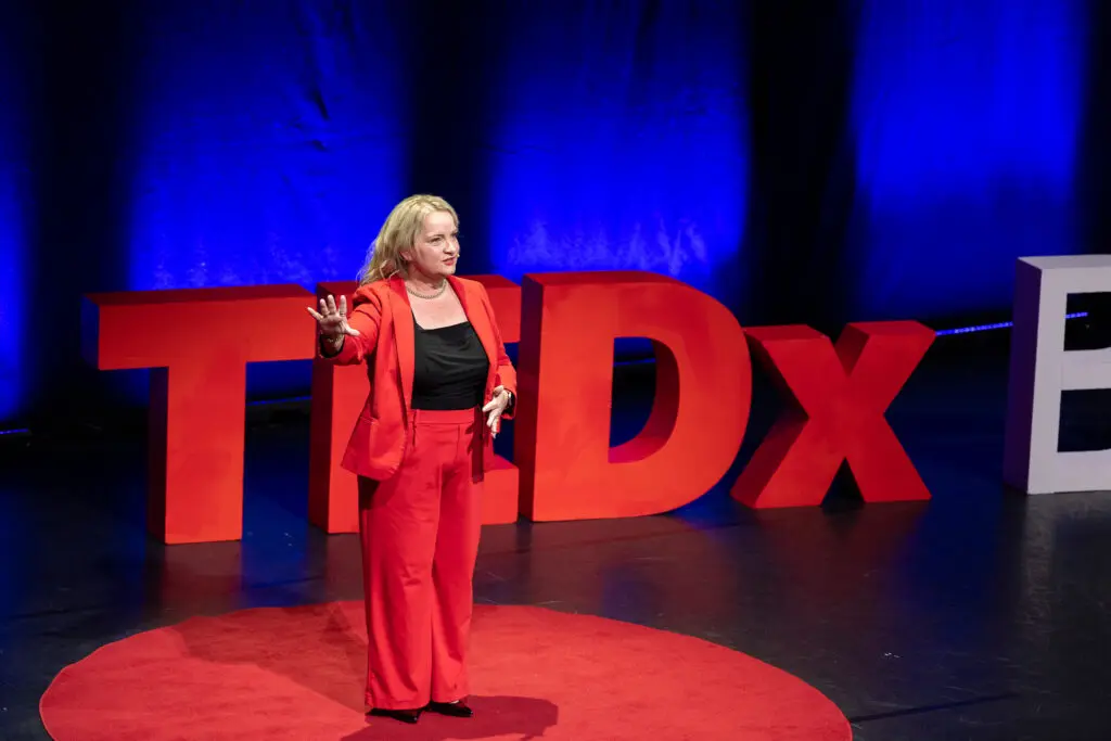 Juanita Wheeler speaking on stage at TEDxBrisbane in a red suit