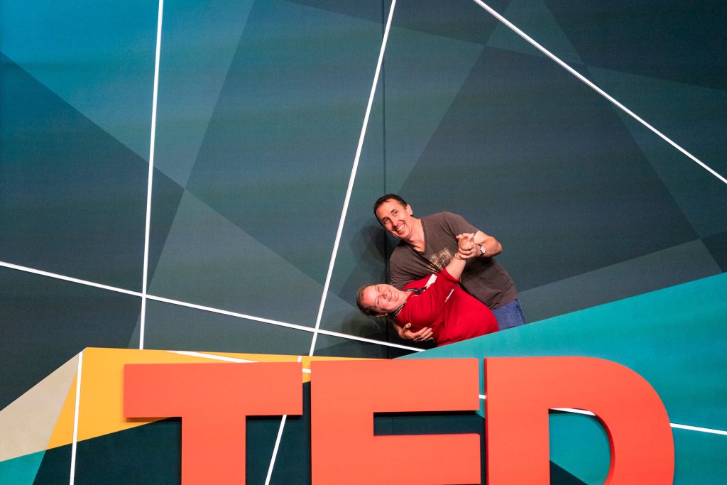 Juanita & Rob at the TED logo Photo Booth stage. Rob holds Juanita in a dance-style dip as they both smile.