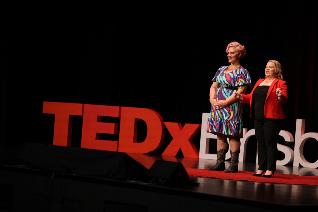 Jenny Wynter and Juanita Wheeler standing on stage explaining the fully improvised TEDx Talk Jenny is about to deliver at TEDxBrisbane.